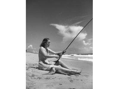 Vintage photo of woman fishing off the beach with 2 large fish at her side